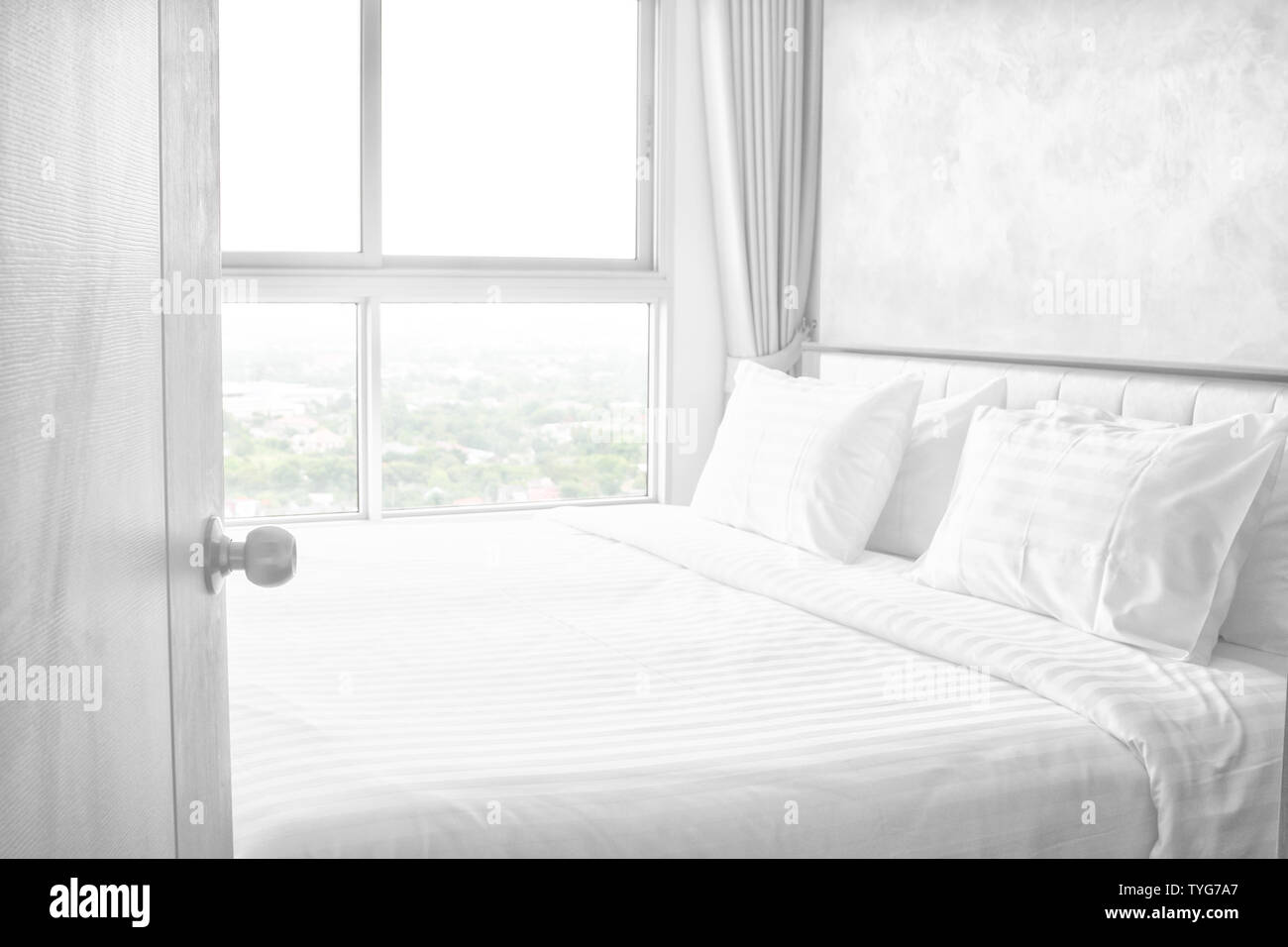 Open Door to bed in hotel room bedroom white bed sheets lit by nature sunlight from view window at morning time Stock Photo