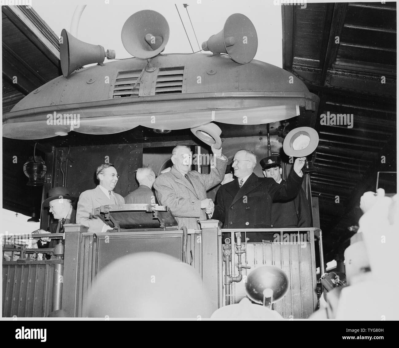 President Harry S. Truman and Vice President-elect Alben W. Barkley standing on the rear platform of the presidential train, waving their hats to the crowd. Truman and Barkley were returning to Washington, DC following their election victory. Stock Photo
