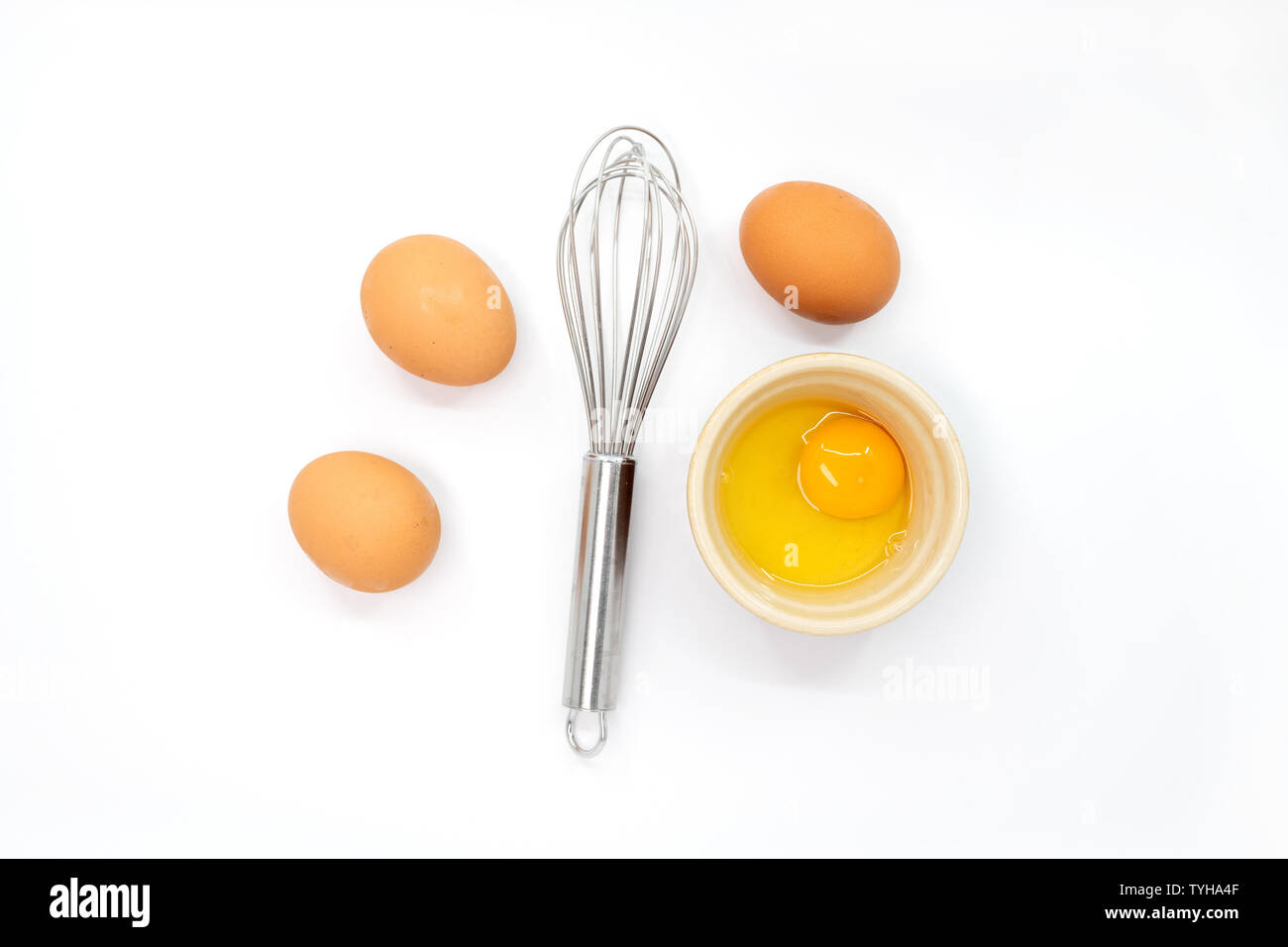 Eggs, a whisk and one egg yolk on a white background Stock Photo
