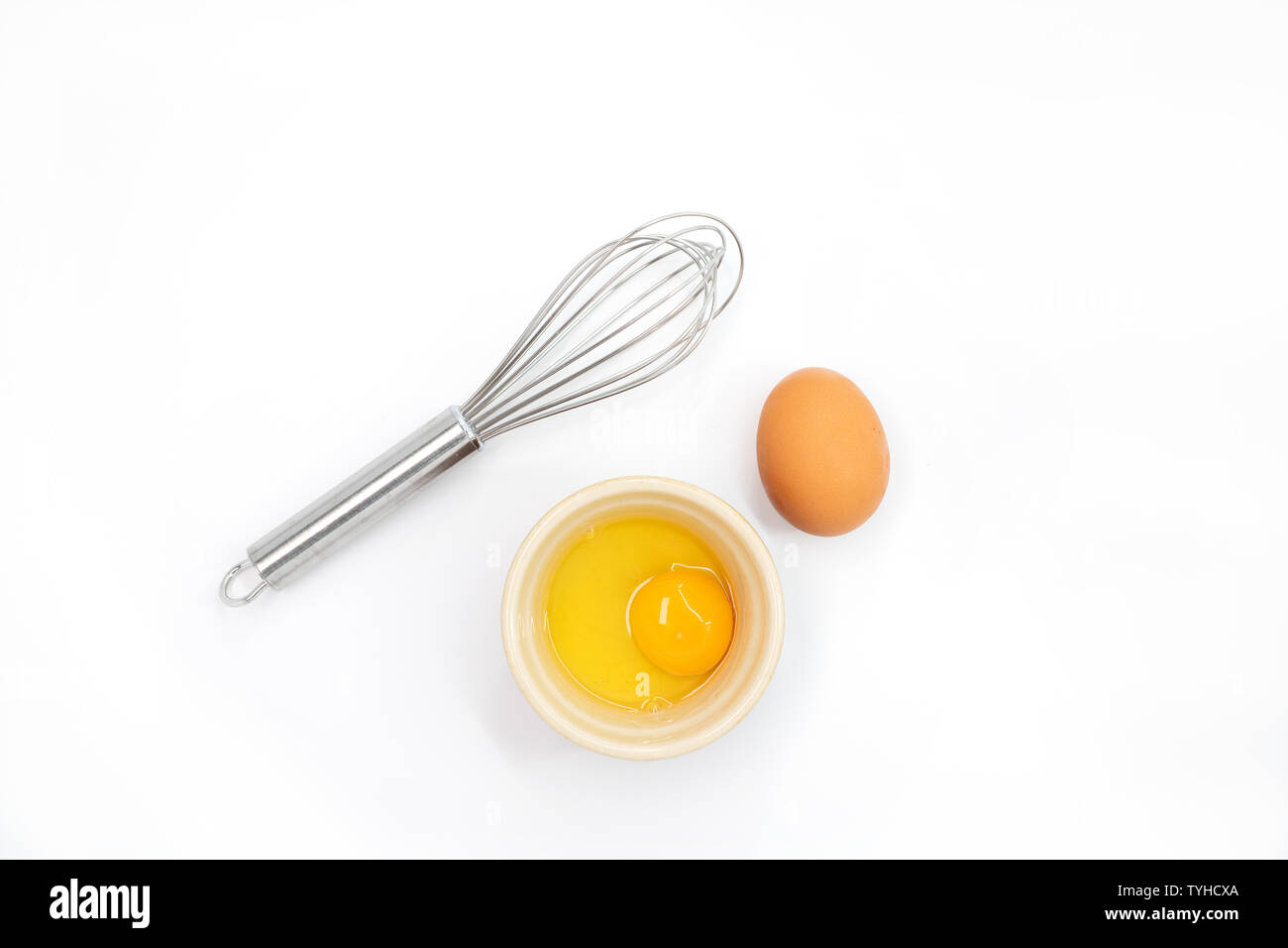 Top view of an egg, egg yolk and whisk on a white background Stock
