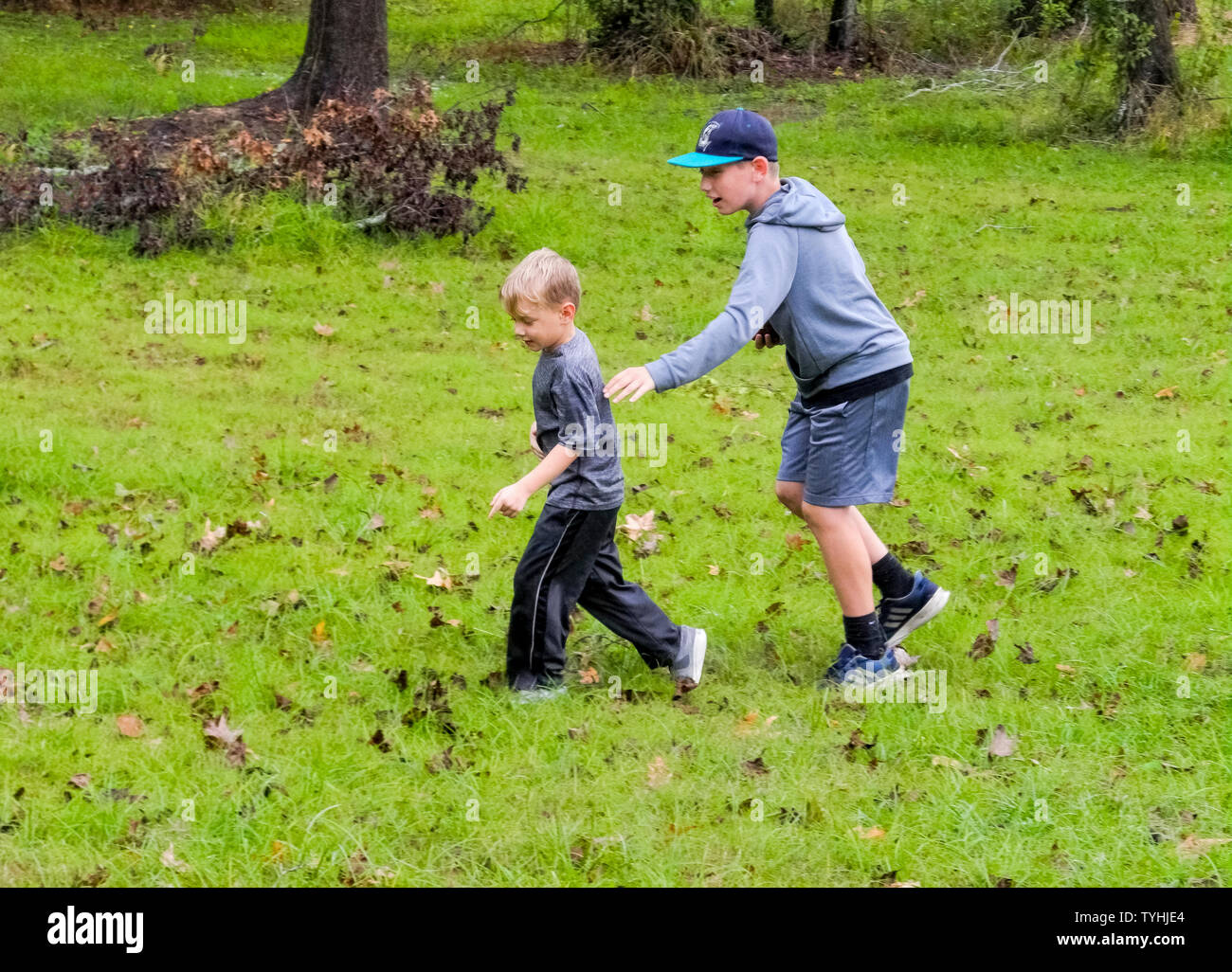 Two young American brothers have fun playing in the grassy backyard of their rural home on an overcast autumn day in Louisiana, USA. Stock Photo