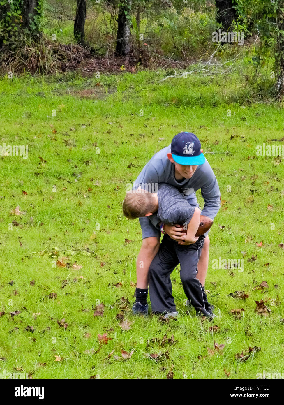 Two young American brothers have fun playing with a football in the grassy backyard of their rural home on an overcast autumn day in Louisiana, USA. Stock Photo