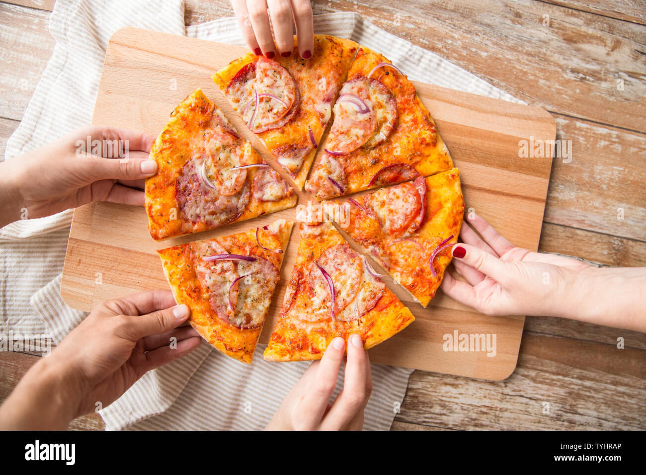 close up of hands sharing pizza on wooden table Stock Photo