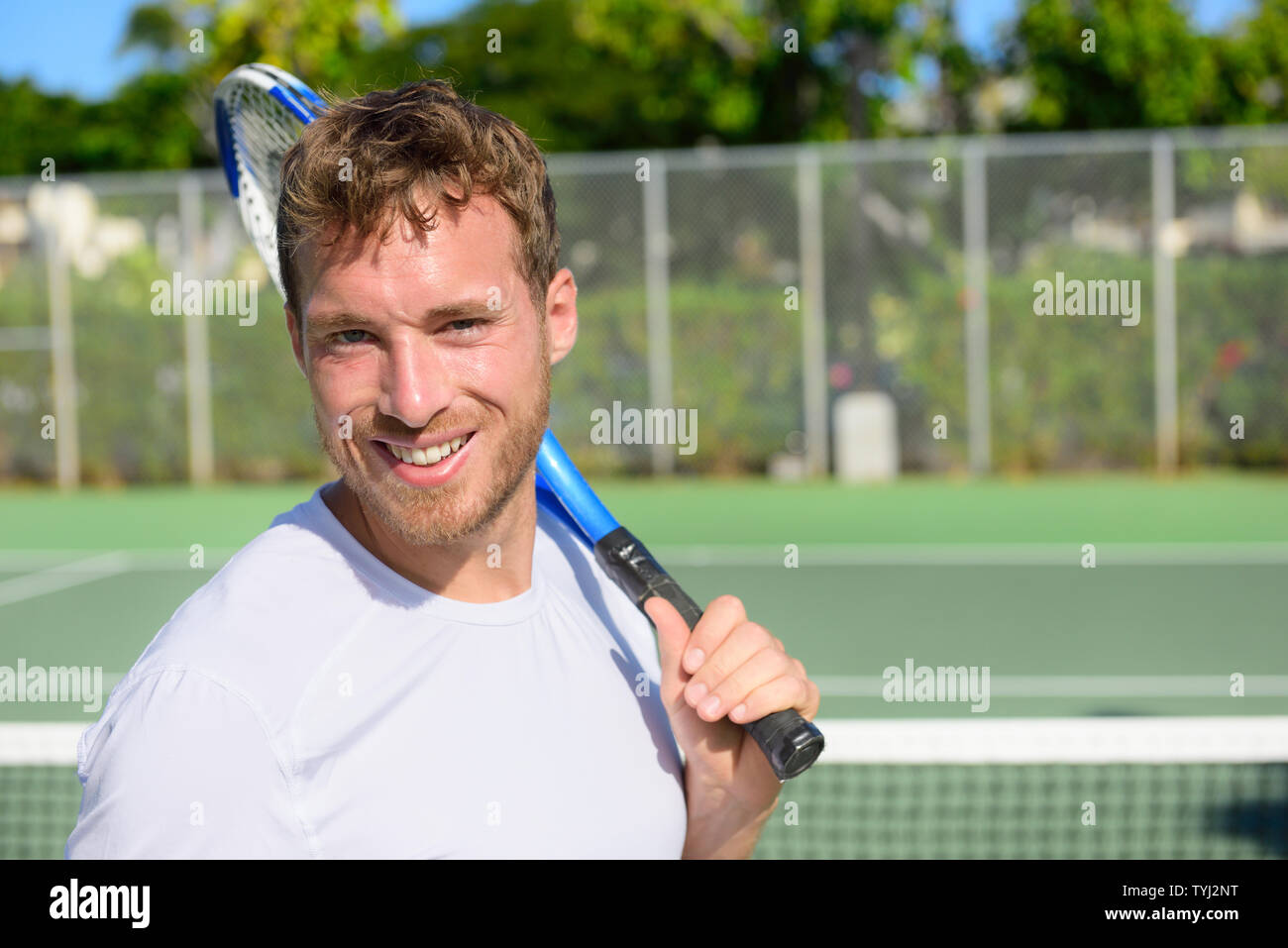 Portrait of male tennis player holding tennis racket after playing at game outside on hard court in summer. Fit man sport fitness athlete smiling happy living healthy active lifestyle outside. Stock Photo