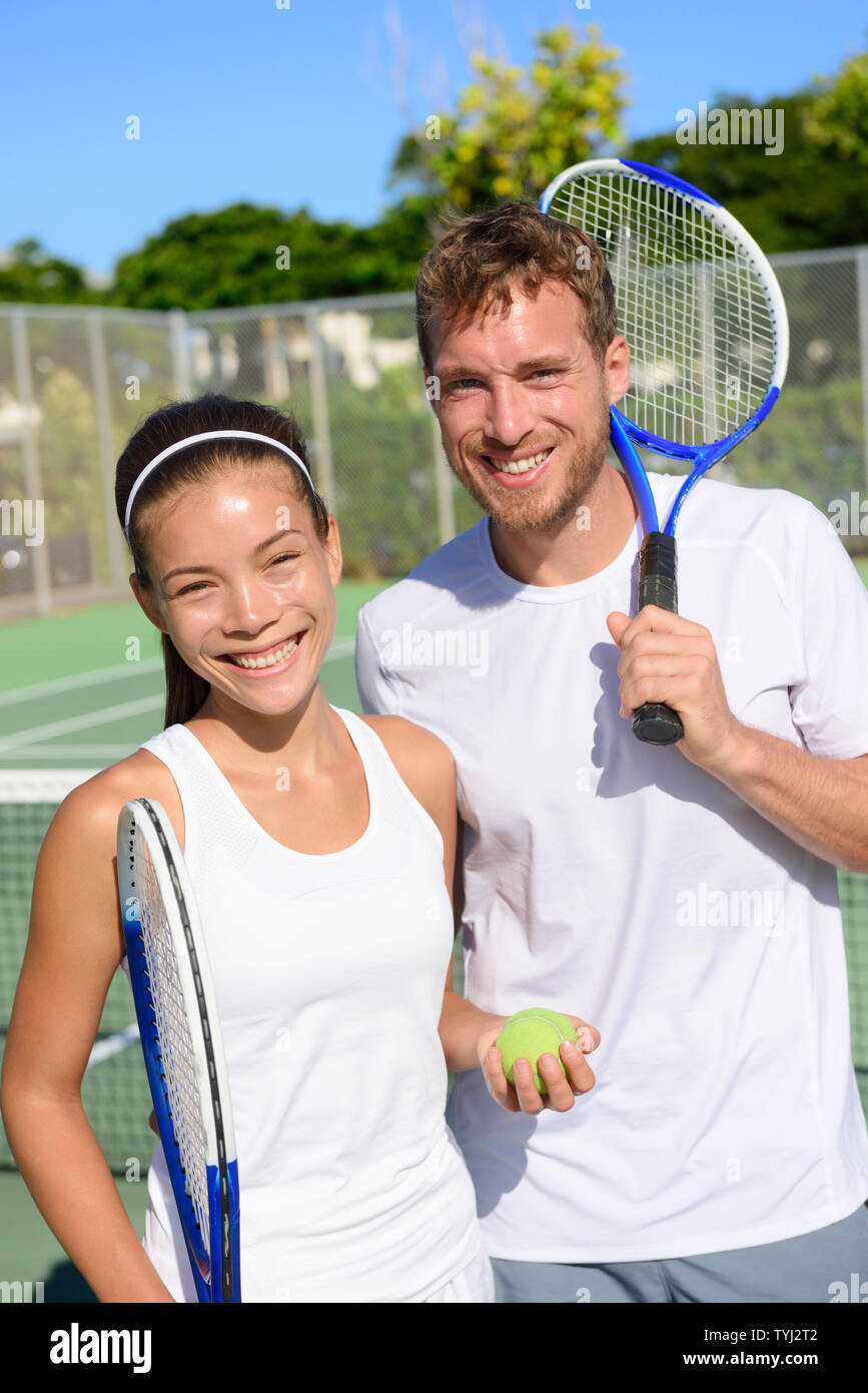 Tennis sport - Mixed doubles couple players portrait relaxing after playing game outside in summer. Happy smiling people on outdoor tennis court living healthy active lifestyle. Woman and man athletes Stock Photo