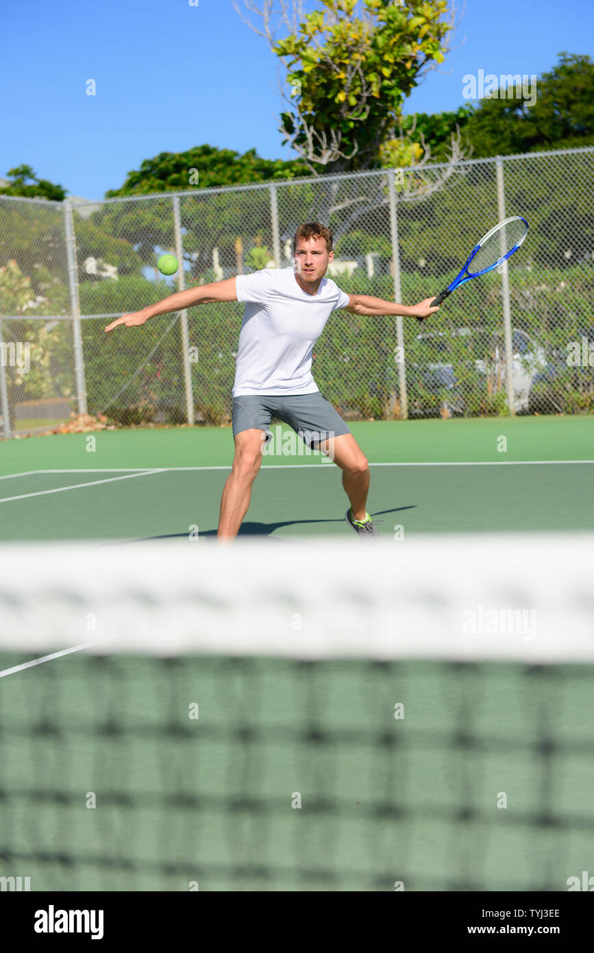 Tennis player - man hitting forehand playing outside on hard court. Male sport fitness athlete practicing in summer outdoors living healthy active lifestyle. Stock Photo