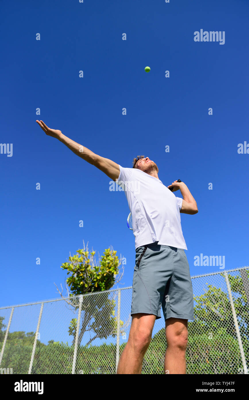 Tennis player serving playing outdoors sport. Man serve with throwing tennis ball up. Male athlete training practicing outdoors in summer. Stock Photo