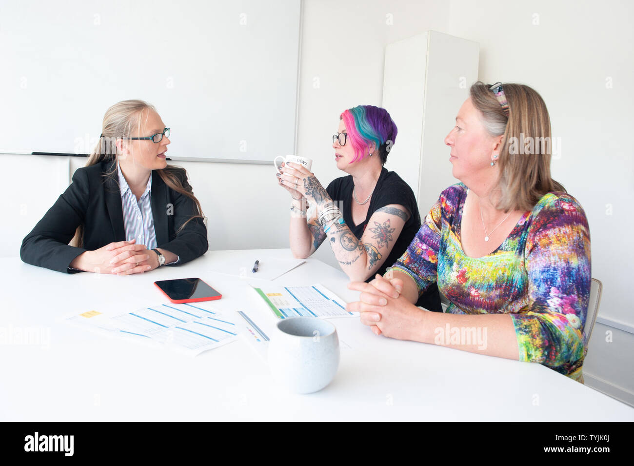 Three women in informal business setting in discussion with paperwork Stock Photo
