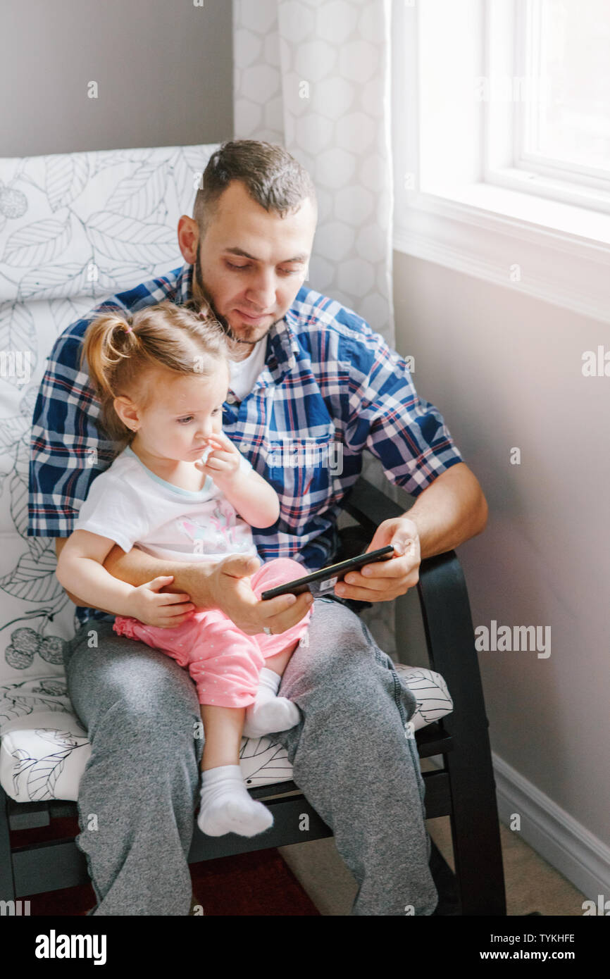 Caucasian bearded father dad sitting with daughter girl child watching cartoons on smartphone digital tablet together. Candid lifestyle family life. S Stock Photo