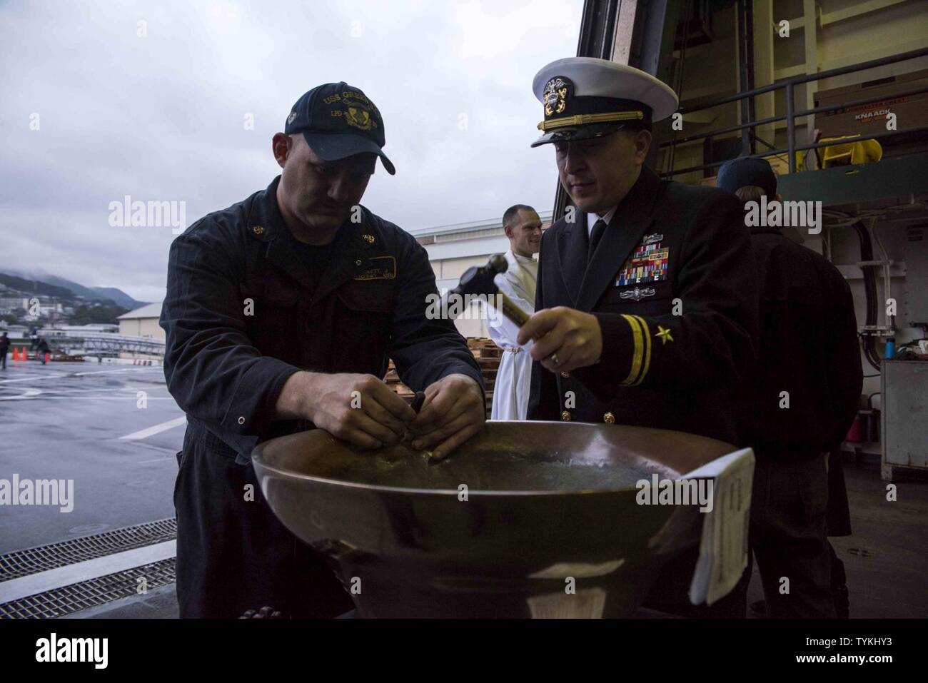 SASEBO, Japan (Nov. 28, 2016) Chief Petty Officer Justin Beckett holds a chisel as Lt. j.g. Brian Caplan hammers a letter of his son’s name into the bell of the amphibious transport dock ship USS Green Bay (LPD 20) during a baptism held in the ship’s hangar bay. Caplan’s son, Theo, was the first newborn to have his name engraved inside Green Bay’s bell. Conducting baptisms and engraving a child’s name into the ship’s bell is a Navy tradition that dates back several hundred years to its origins in the British Royal Navy. Green Bay, forward-deployed to Sasebo, Japan, is serving forward to provid Stock Photo