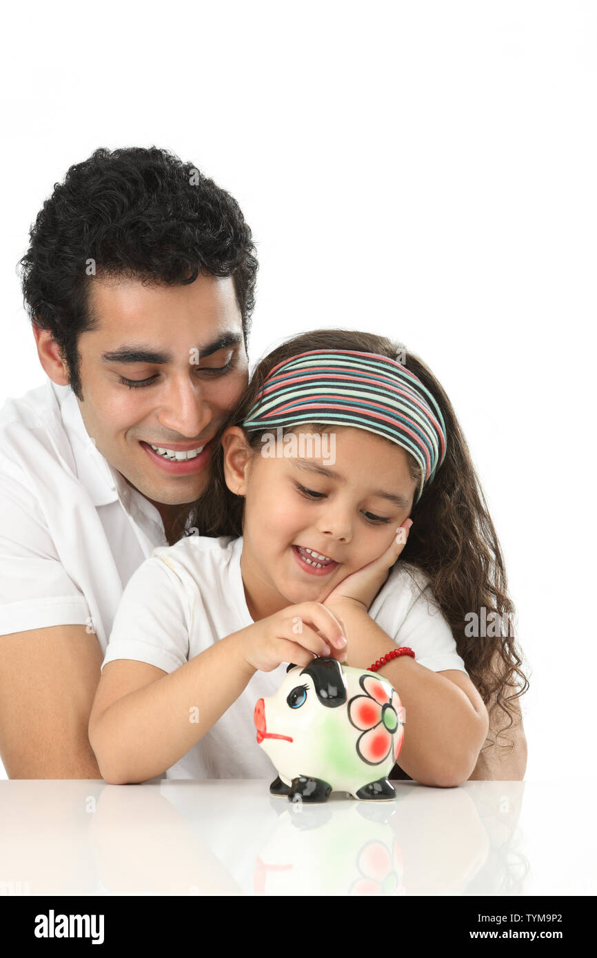 Girl putting coin into a piggy bank with her father Stock Photo - Alamy