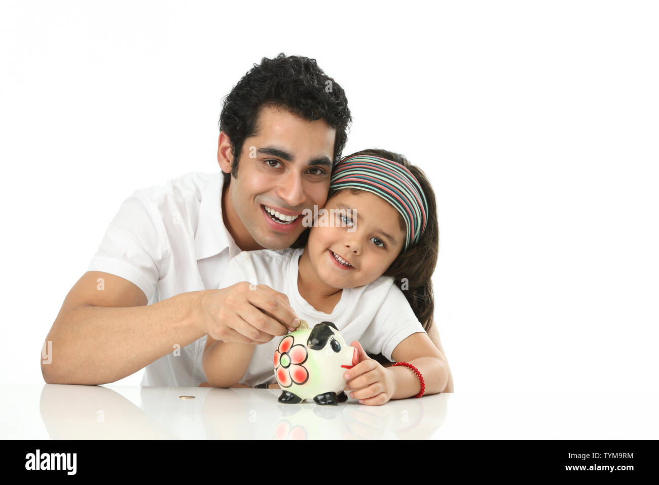 Girl putting coins into a piggy bank with her father Stock Photo - Alamy