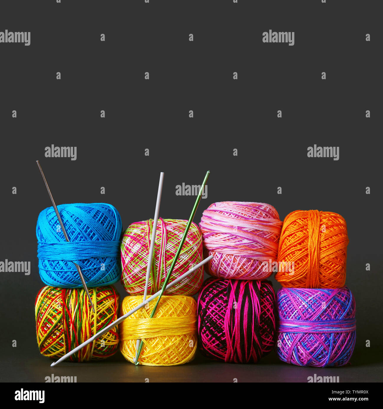 A stack of colorful yarn coils and needles over grey background Stock Photo
