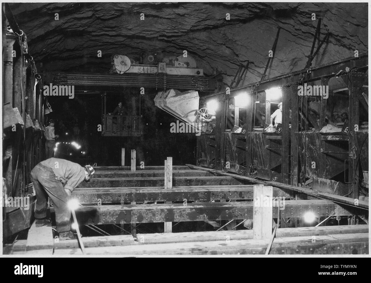 Traveler crane handling dump bucket at top of side-wall forms in diversion  tunnel No. 2. Concrete is dumped from bucket into hopper which is then  lifted by cable, dumping concrete behind form.