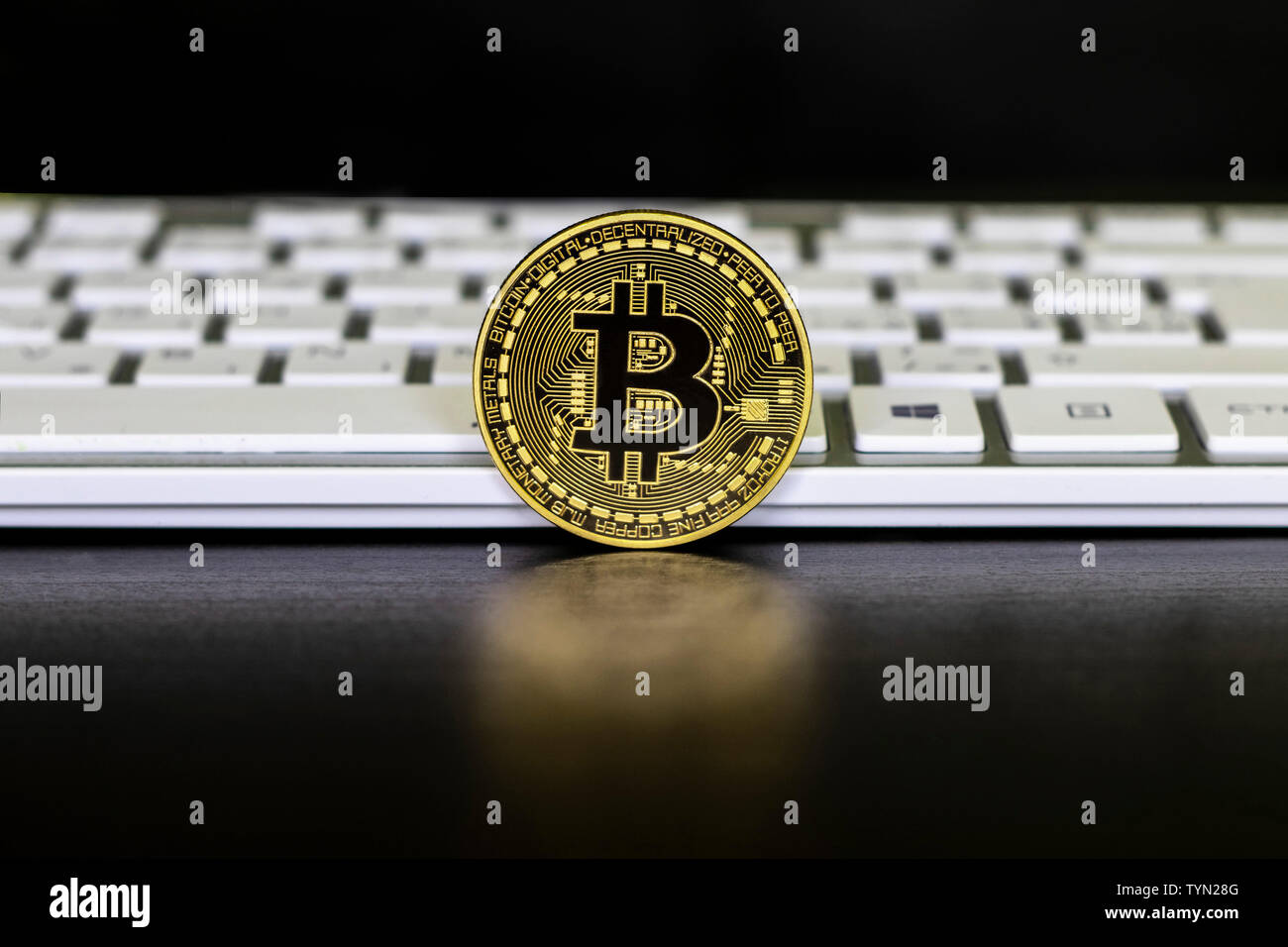 The gold coin of the bitcoin stands on the black background in front of the  white keyboards. Bitcoin is the best-known crypto currency Stock Photo -  Alamy