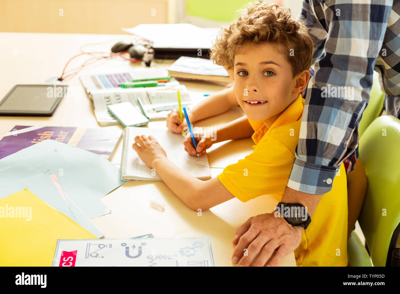 Doing an exercise. Positive cute boy smiling while writing in his ...