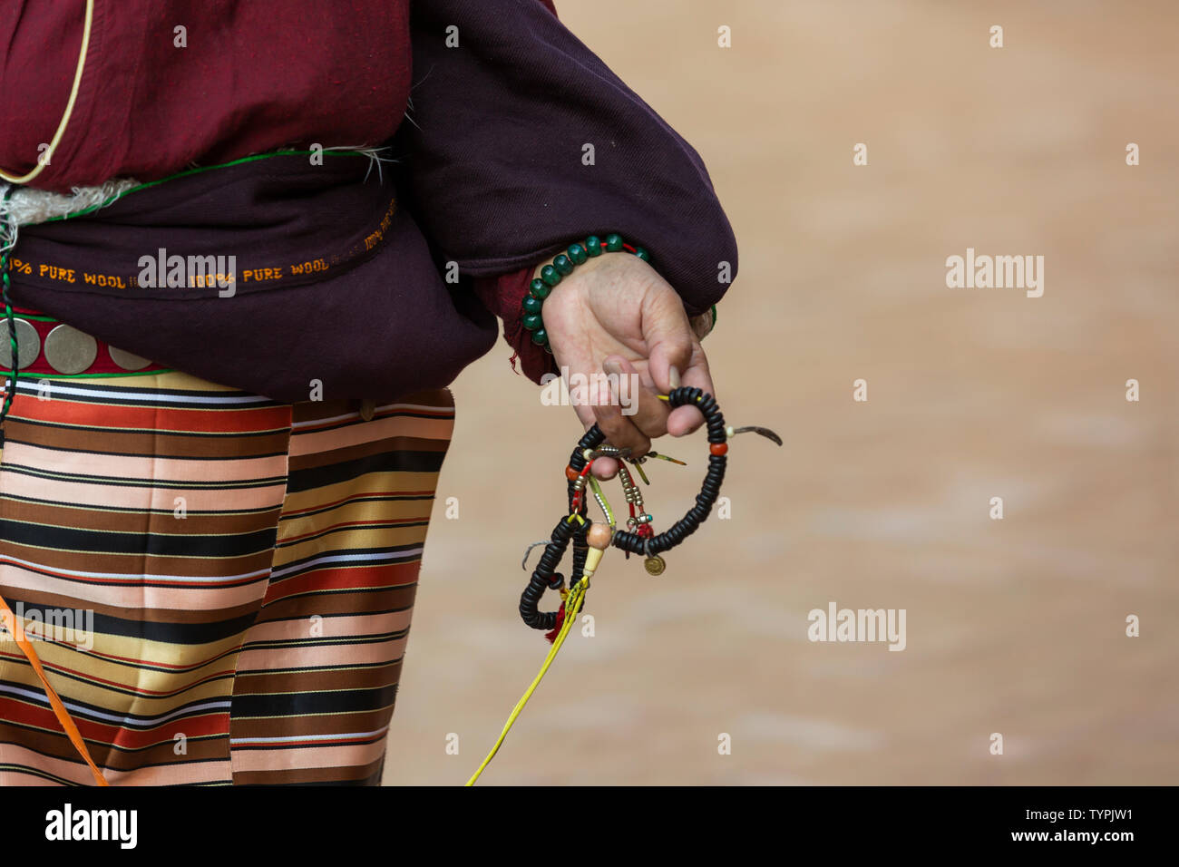 close up of a women, wearing traditional Tibetan clothes, and holds a prayer chain in her hand Stock Photo