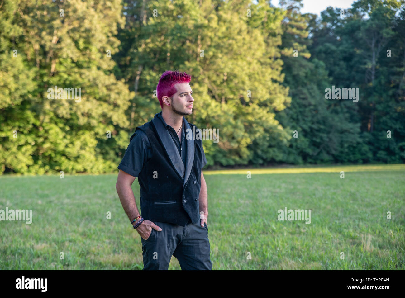 Alternative white caucasian man with pink hair outside gazing in the distance, contemplative. Trees in the background with blank empty room space for Stock Photo