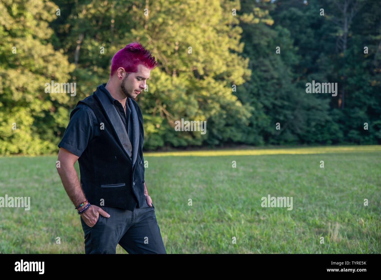 Diverse alternative looking white male caucasian with spkiy pink hair staring down at the ground. Feeling depressed, sad, or defeated. Pierced brow. Stock Photo