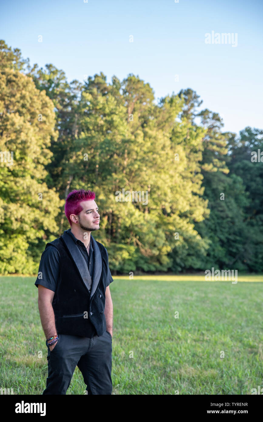 Alternative white caucasian man with pink hair outside gazing in the distance, contemplative. Trees in the background with blank empty room space for Stock Photo