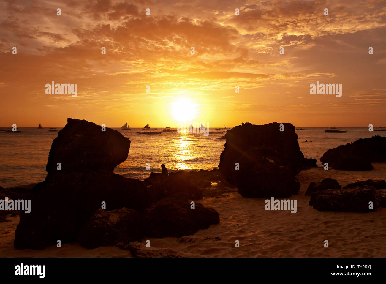 big rocks on beach at sunset with boats in sea in background, Boracay island, the Philippines Stock Photo