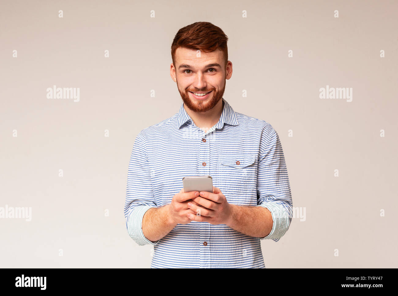 Young bearded man using his phone and smiling Stock Photo