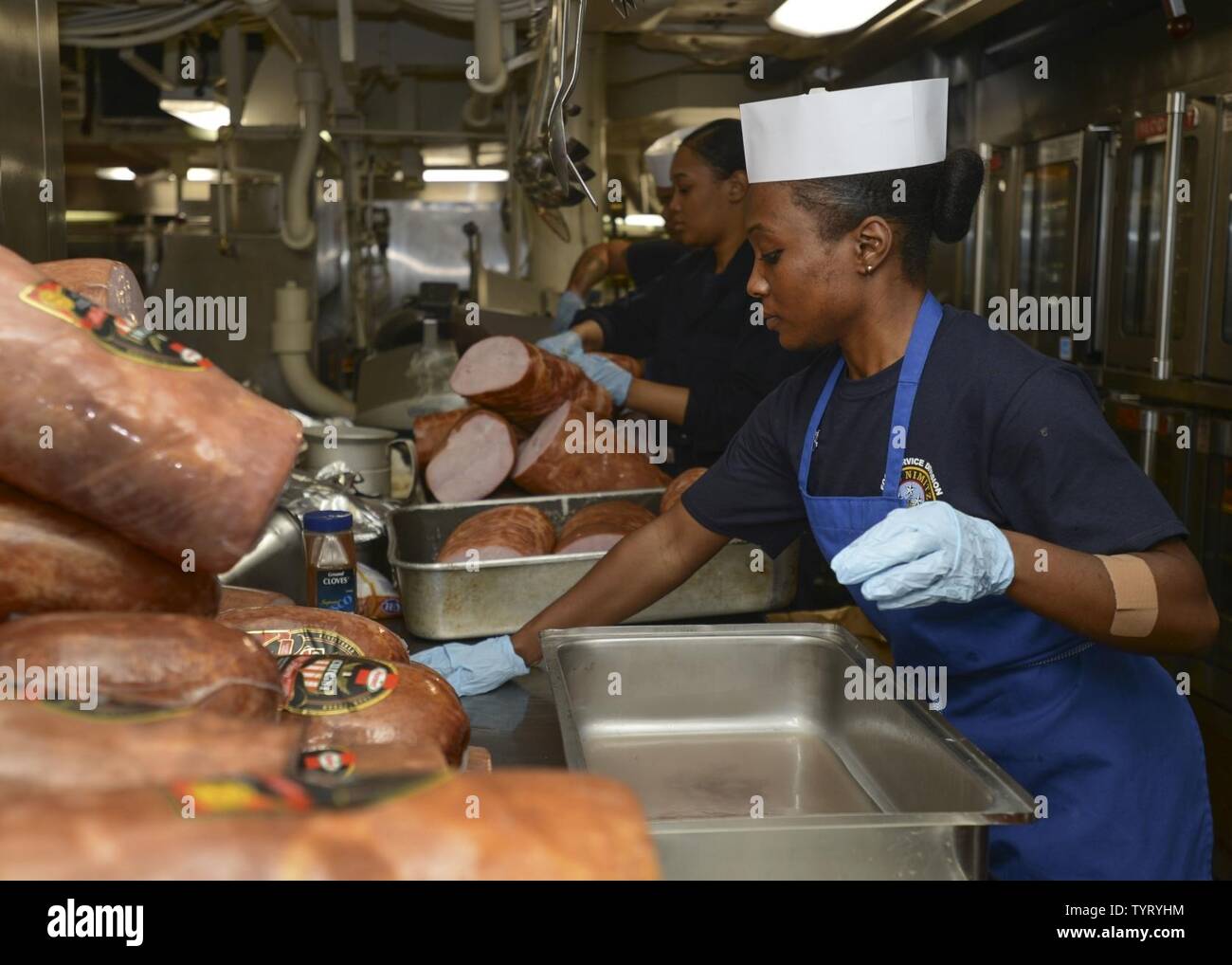 PACIFIC OCEAN (Nov. 24, 2016) Sailors assigned to the aircraft carrier USS Nimitz (CVN 68) prepare ham in the galley for a Thanksgiving celebration. Nimitz is currently underway conducting Tailored Ship's Training Availability and Final Evolution Problem (TSTA/FEP), which evaluates the crew on their performance during training drills and real-world scenarios. Once Nimitz completes TSTA/FEP they will begin Inspection and Survey (INSURV) and Composite Training Unit Exercise (COMPTUEX) in preparation for an upcoming 2017 deployment. Stock Photo