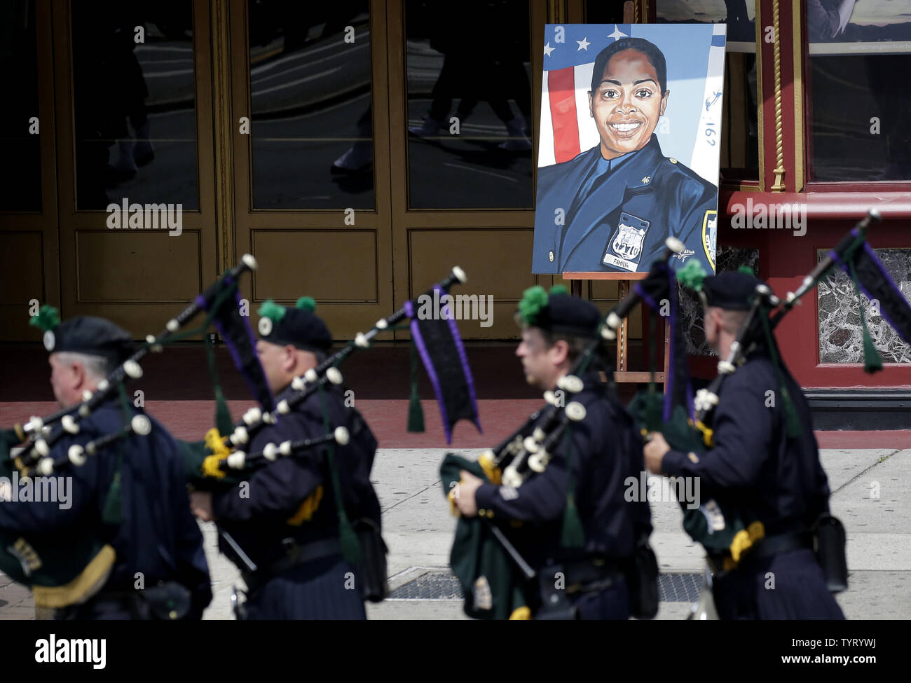 Bag Pipers march by a portrait of Police officer Miosotis Familia outside of her funeral at