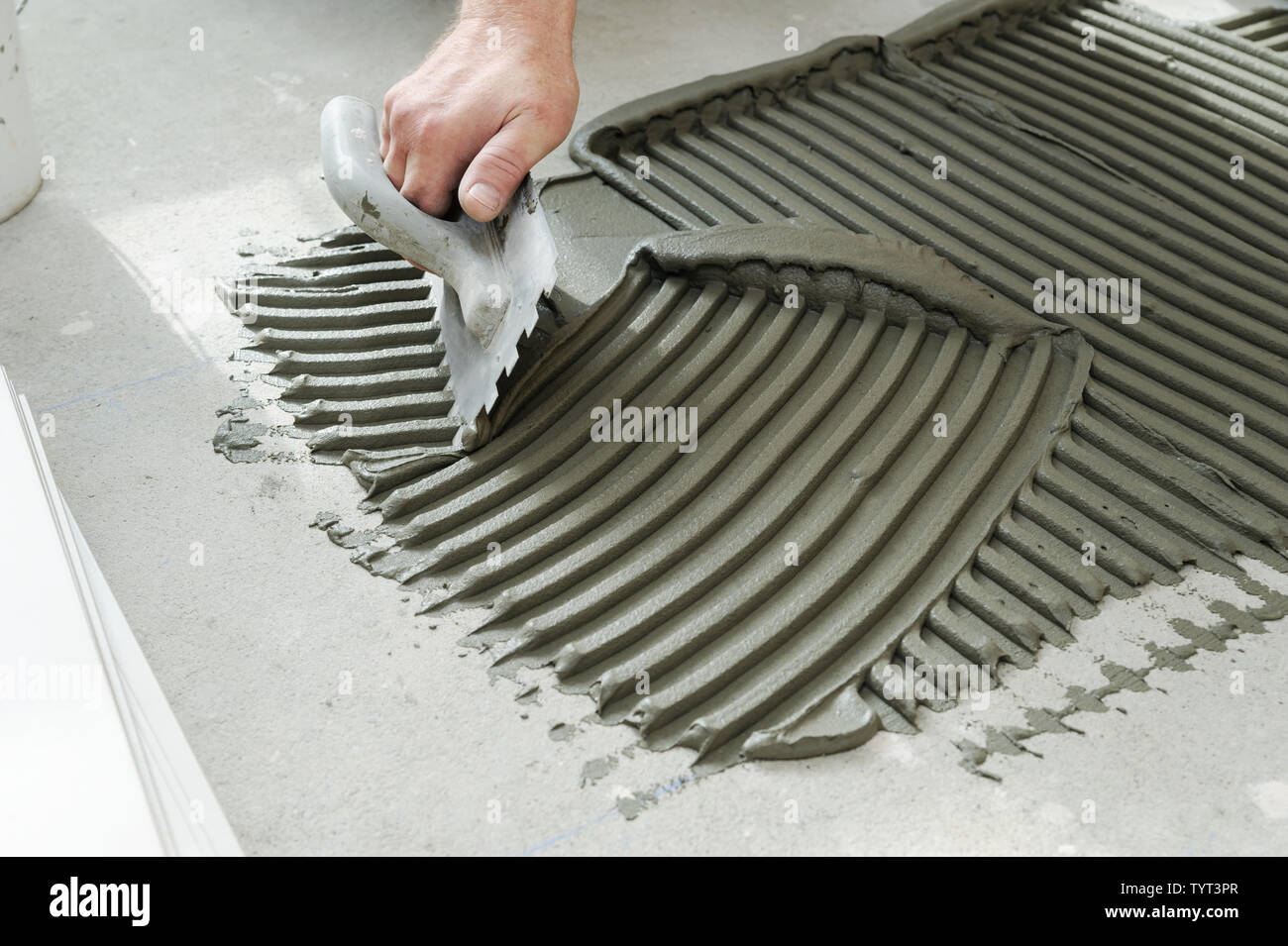 The hand of a tiler is putting tiles adhesive to the wall with the