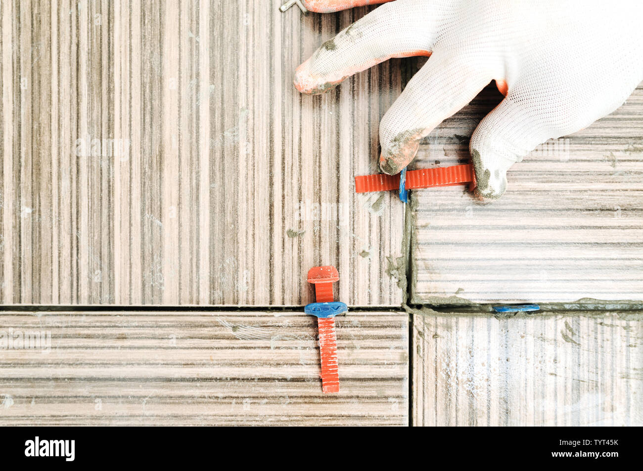 Tiler's hand is using plastic wedges and clips for aligning tiles