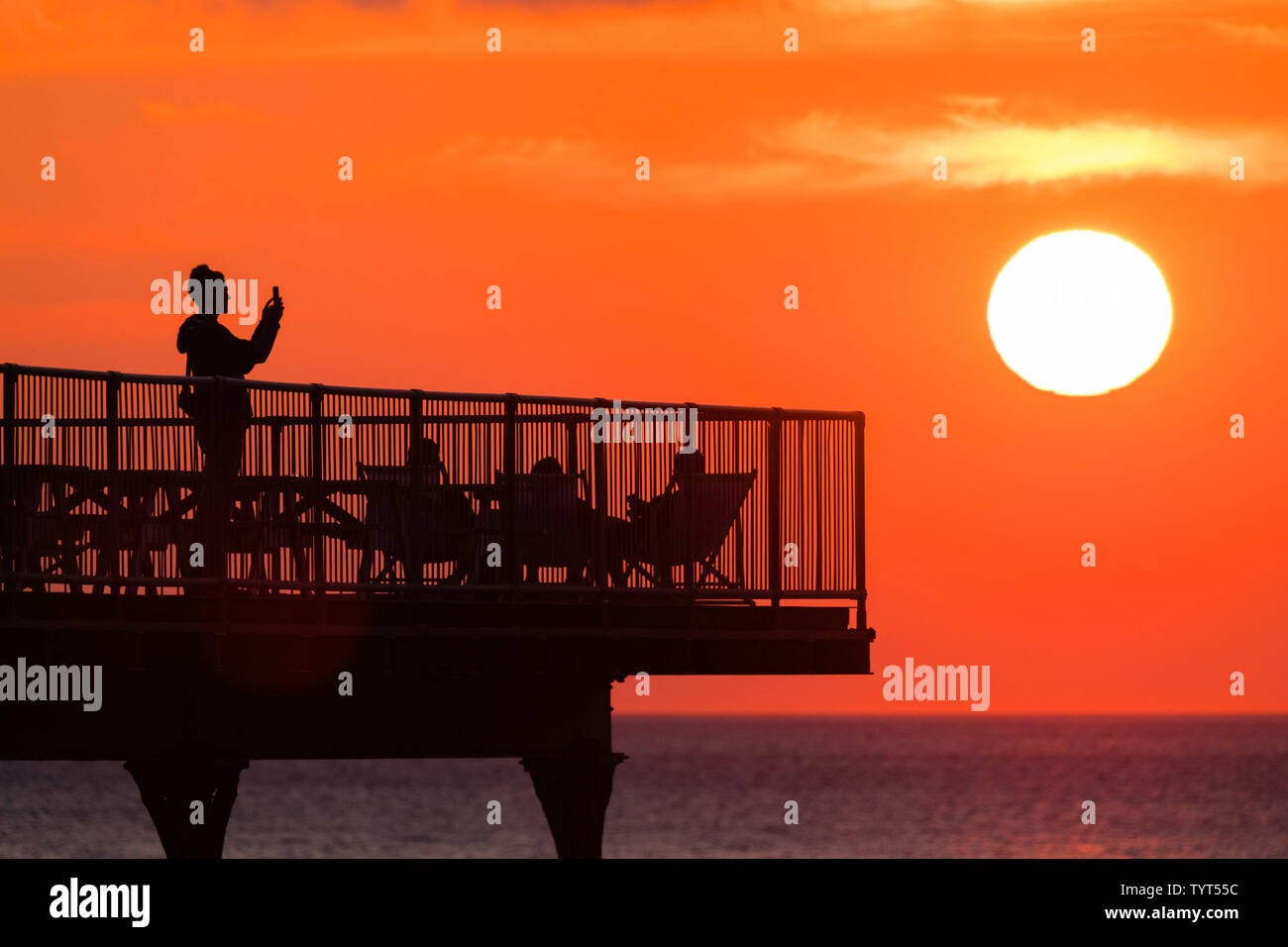 Aberystwyth Wales UK, Wednesday   26 June 2019  UK Weather: People  on the pier watching the glorious sunset in Aberystwyth on the Cardigan Bay coast, west Wales, as the country heads into a spell of fine weather and the hottest days of the summer so far,  with temperatures expected to reach the high 20’s centigrade   photo credit: Keith Morris/Alamy Live News Stock Photo
