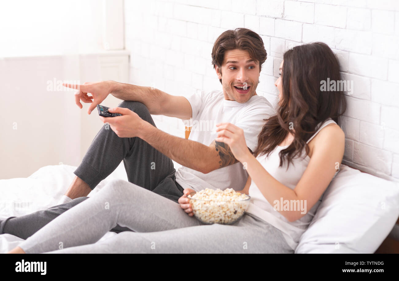 Millennial couple watching movie with popcorn, sitting in bed Stock