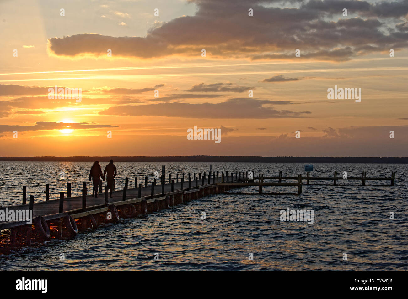 Couple walking on wooden jetty at sunrise. Stock Photo