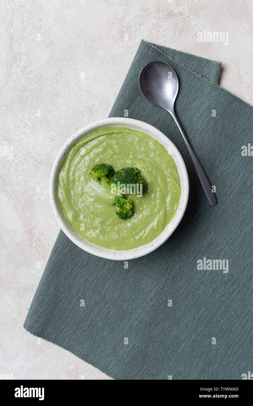 Tasty broccoli cream soup in white bowl on green napkin at bright table. Concept of healthy, fasting food. Above view Stock Photo