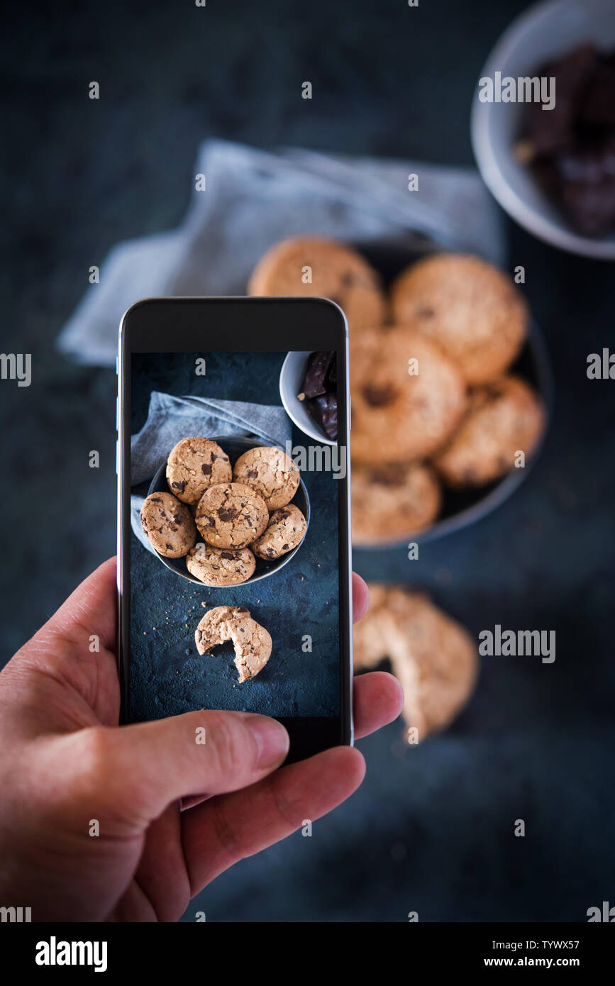 Person taking picture with a phone to some cookies with chocolate.Cookies with chocolate chips and hazelnuts. Stock Photo