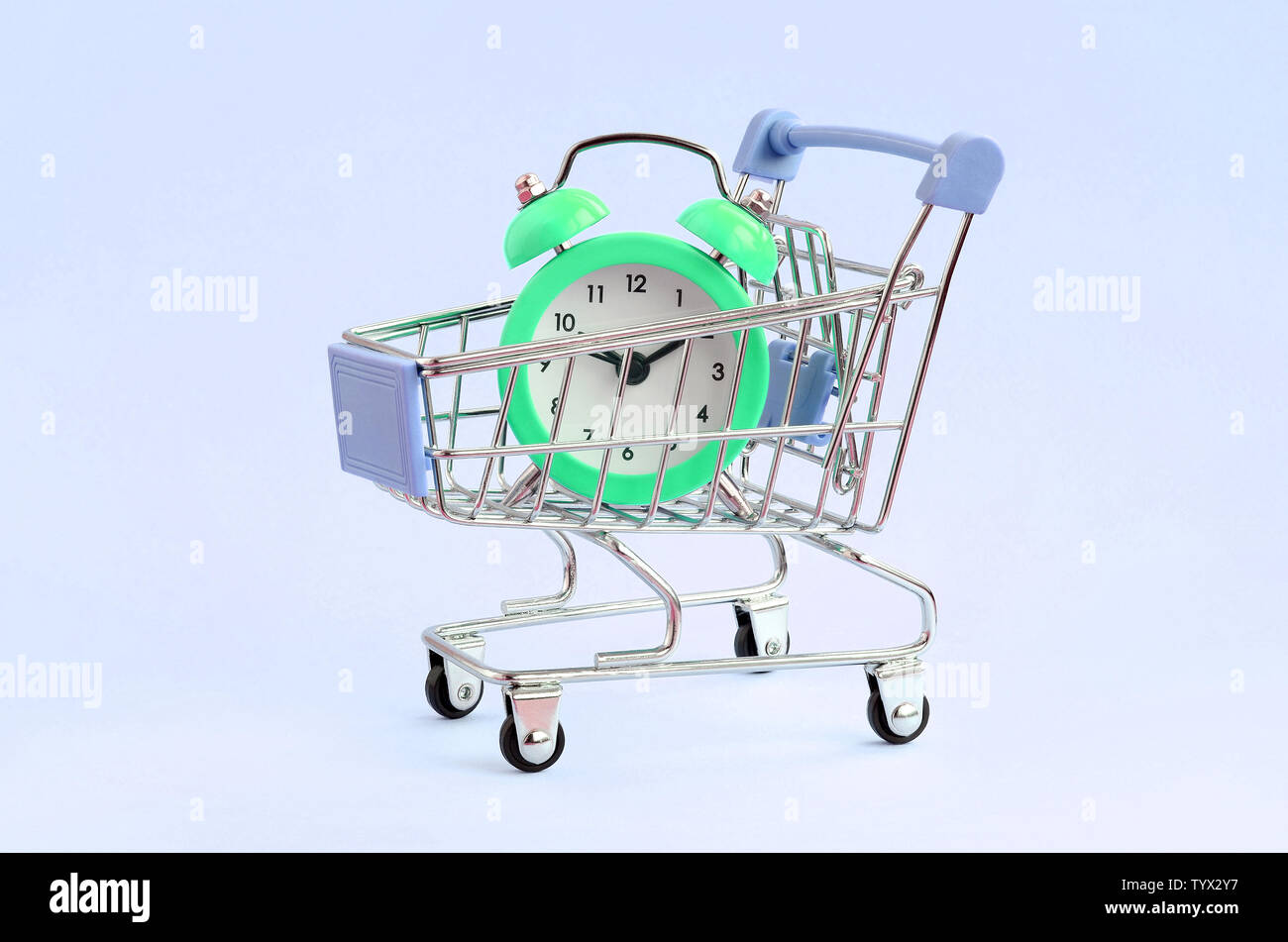 Green alarm clock in supermarket trolley on blue background. Time resource acquisition concept