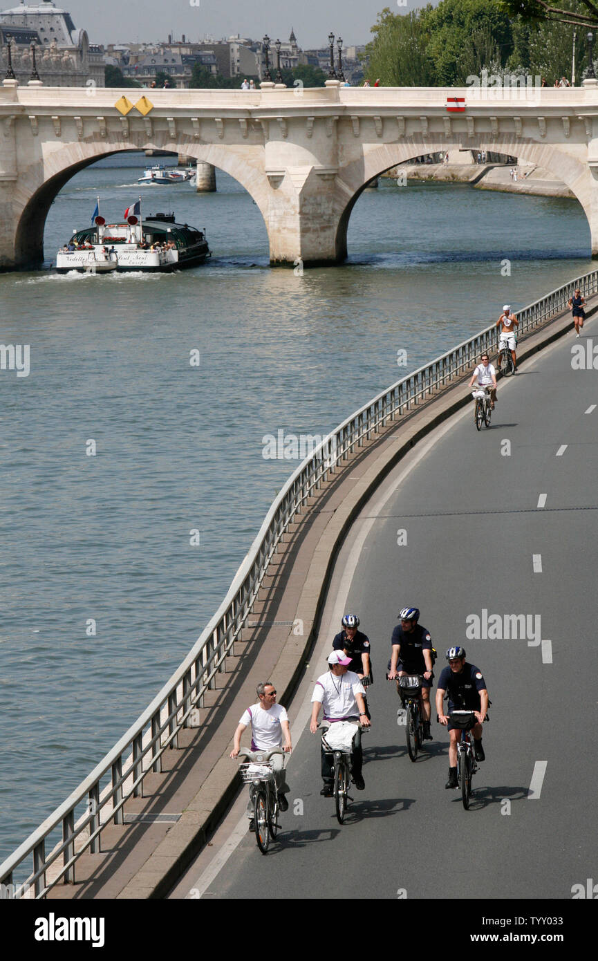 Two riders, escorted by police, ride along the Seine river after being among the first to rent a bicycle following the official launch of the 'Velib' citywide bicycle program in Paris on July 15, 2007.  Parisians and visitors can rent a bicycle free of charge for the first half hour from among the new fleet of 20,000 that will be available from approximately 750 automatic kiosks around the city.   (UPI Photo/ David Silpa) Stock Photo