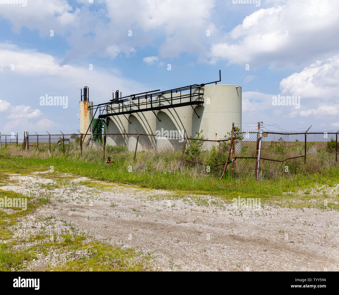 Old oil well storage tanks in farm field. Oil well abandonment, environment pollution, and oil production concept Stock Photo