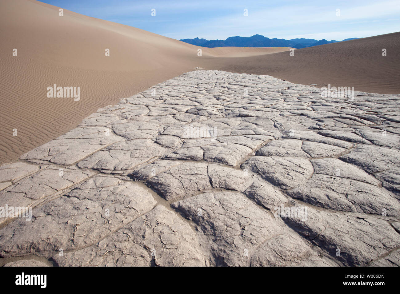 Mudcracks (dessication cracks) on dry lake bed surrounded by sand dunes in the Mojave Desert, Death Valley National Park, California, USA Stock Photo