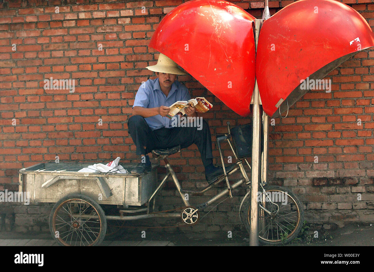 A Chinese delivery man shelters from the midday sun under a phone booth  as he reads a magazine in central Beijing, August 2, 2006.  Officials are examining new steps to cool off China's sizzling economy as its top planning agency called for tighter bank credit and curbs on construction, state media reported.  The reports Wednesday suggested Beijing believes earlier measures, including an interest rate rise in April, are failing to contain runaway growth in spending on factories and other assets that Chinese leaders worry could ignite a financial crisis.  (UPI Photo/Stephen Shaver) Stock Photo