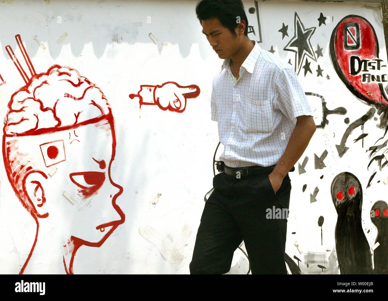 A Chinese man walks by a wall of graffiti, some political, in downtown Beijing, May 23, 2006.  As personal incomes continue to rise, as well as access to the outside world via the internet and more relaxed censorship of movies and magazines, many Chinese youth have taken to music, blogs and art to express themselves in ways previously banned.   (UPI Photo/Stephen Shaver) Stock Photo