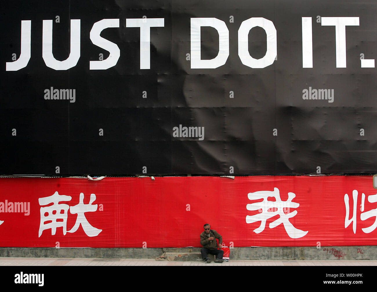 A Chinese man sits in front of a huge Nike advertisement outside a shopping  mall in Beijing, China on April 28, 2008. The Beijing 2008 Olympics are  fast approaching and one of