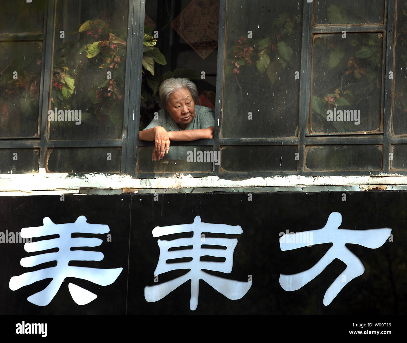 An elderly Chinese woman looks out her window above a trendy clothing store for young women in Beijing, September 11, 2010.  The proportion of people above 65 in China will surpass that of Japan in 2030, which will make China the world's most aged society, according to the Chinese Academy of Social Sciences.  The problem with an increase in China's elderly population is that it will slow GDP per capita growth, investment and capital accumulation, while at the same time increasing public debt.      UPI/Stephen Shaver Stock Photo