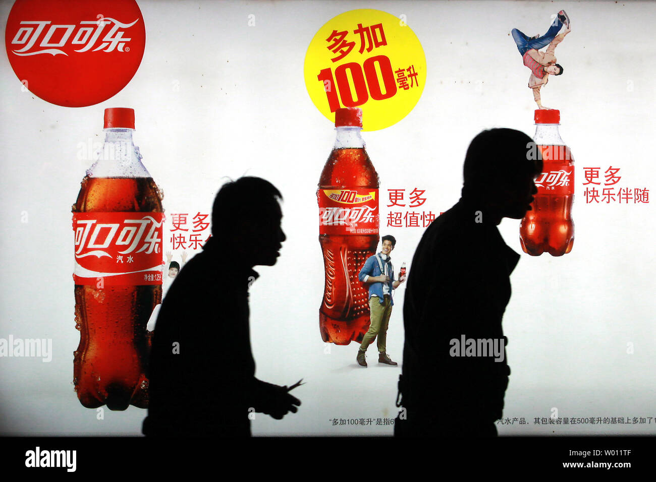 A Chinese walk past a billboard advertising Coca-Cola soft drinks on the streets of Beijing on October 23, 2012.  Last week Coca-Cola said that sales in China grew an anemic 2% compared to 11% last year.  Shares of the world's largest beverage company lost more than 2% this month, mainly due to the slowing of China's economy.      UPI/Stephen Shaver Stock Photo