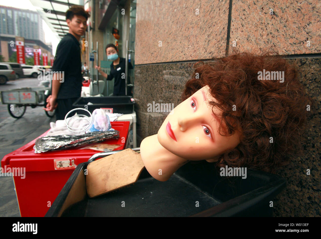 A Western-looking mannequin's head attached to a hair brush lays on a cart  outside a Chinese hair salon in Beijing on July 14, 2013. Modern, Western hair  styles, along with being 'blond',