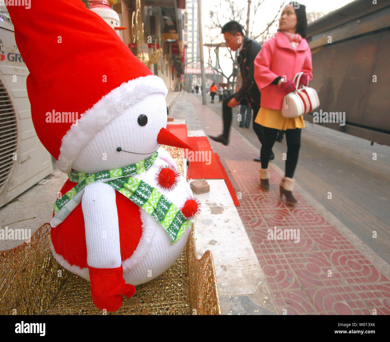 Chinese walk past a clothing store advertising its holiday sales with the help of a 'snowman' outside its doors in Beijing on December 8, 2013.  Western holidays, regardless of their religious and cultural significance, are growing in popularity among China's emerging middle class as the country continues to open up to Western culture.     UPI/Stephen Shaver Stock Photo