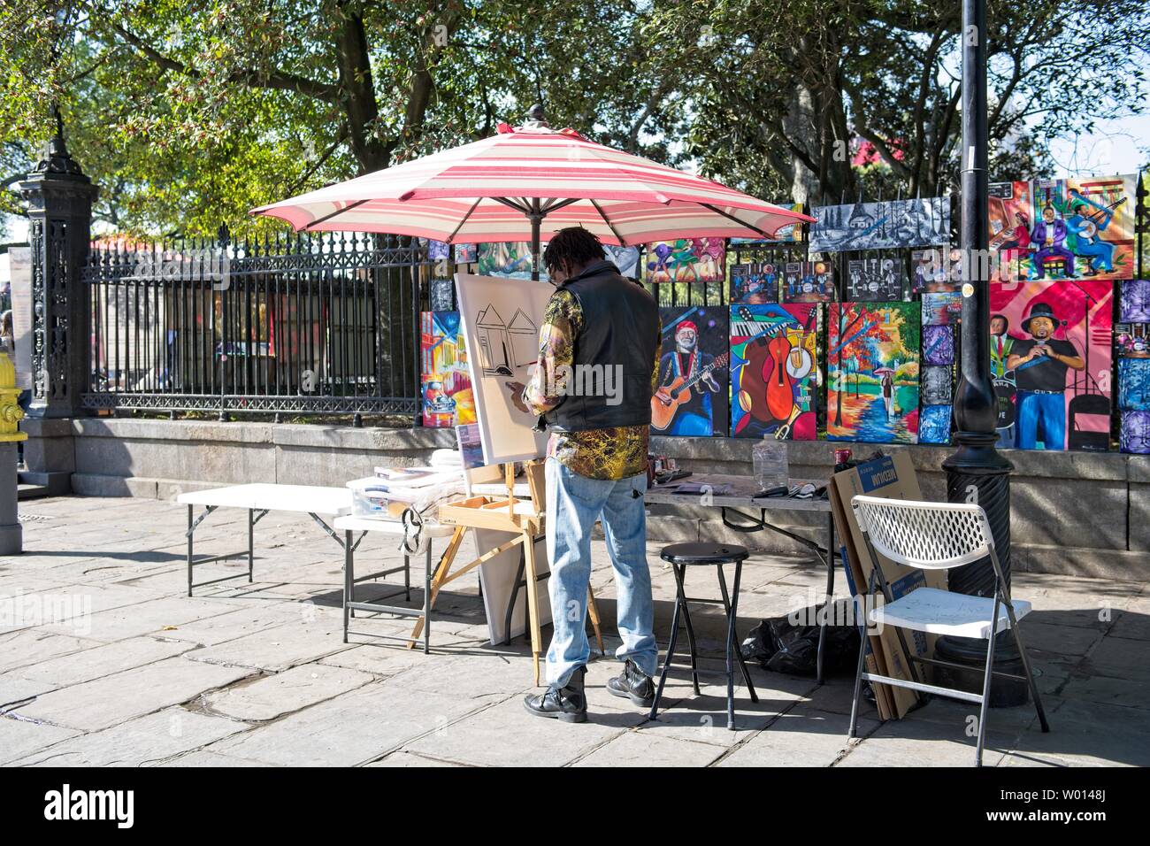 An artist and street vendor paints his art on the streets near a park