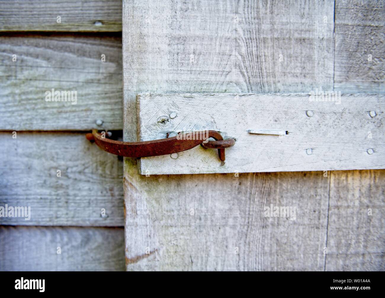A rusted handmade latch keeps a gate closed on a weathered wooden fence