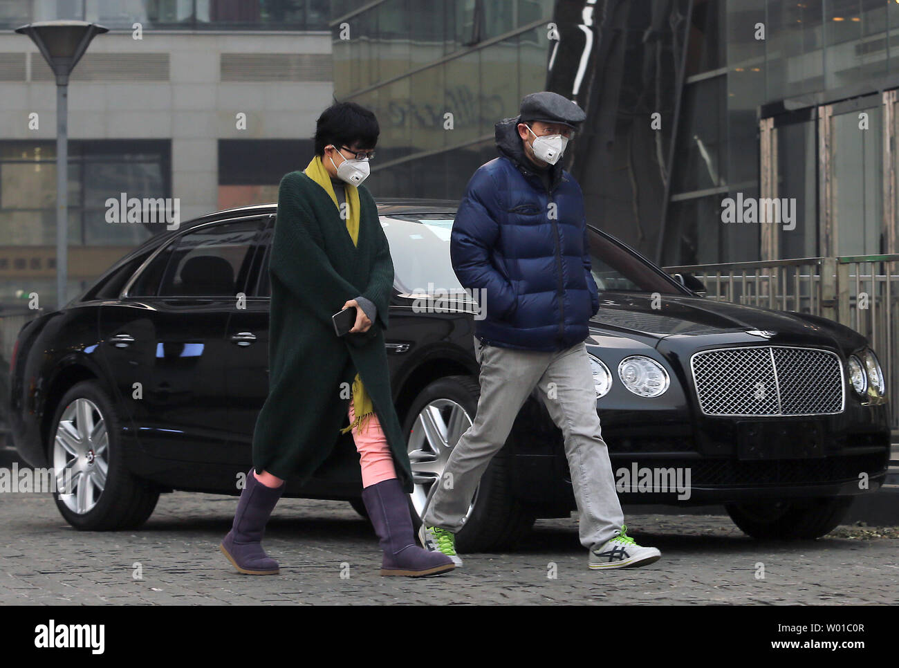 Chinese wearing respirator masks walk past a new Bentley outside a showroom in downtown Beijing on December 3, 2016.  China has imposed a 10 percent tax on ultra high-end luxury cars costing over $190,000 such as Ferraris, Bentleys, Aston Martins, Maseratis, Lamborghinis and Rolls-Rocye cars in a nationwide crackdown on conspicuous consumption and graft, while promoting more fuel-efficient vehicles.         Photo by Stephen Shaver/UPI Stock Photo