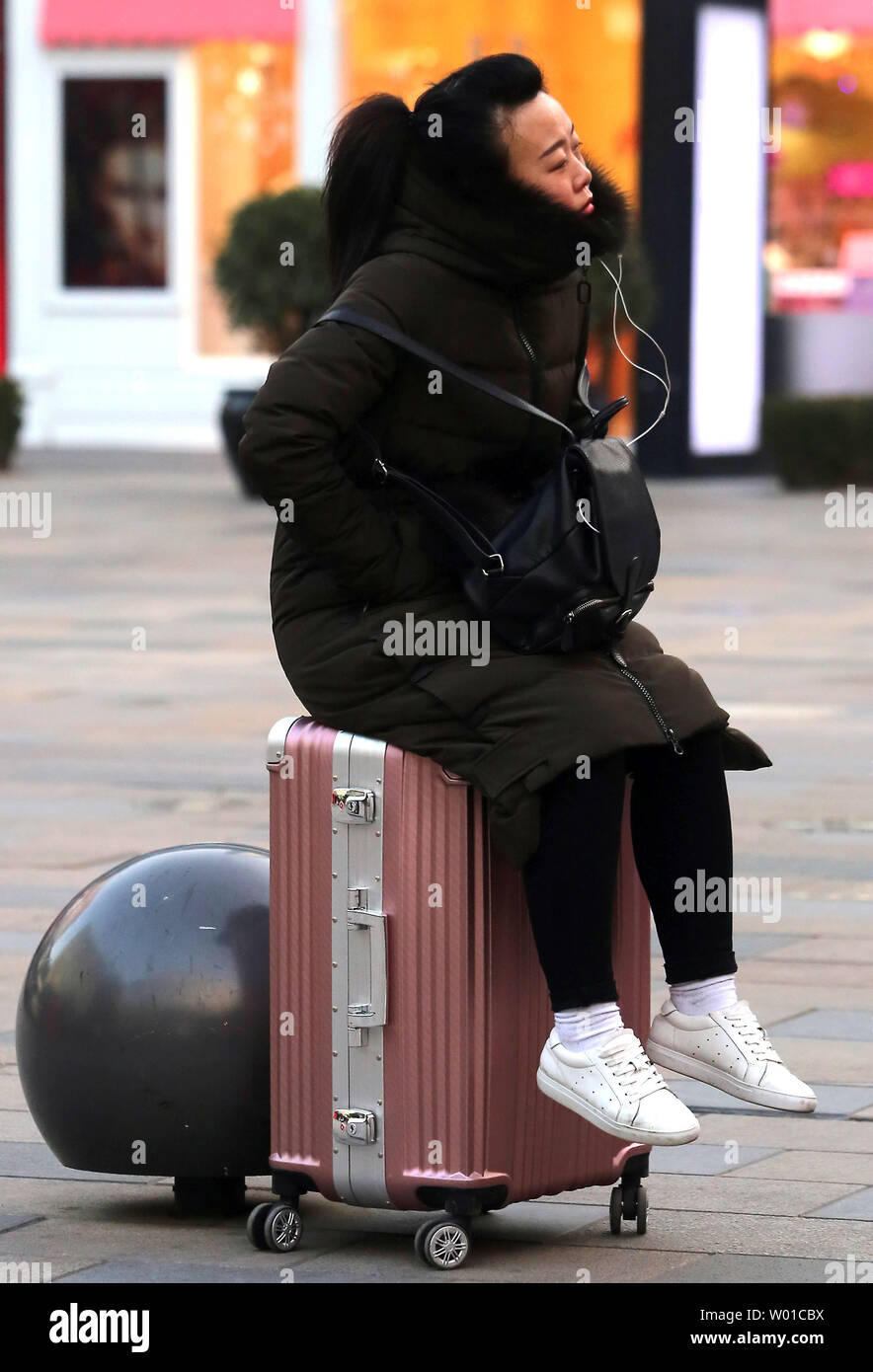 A Chinese woman sits on a suitcase outside an international trade mall in Beijing on February 6, 2017.  Reports from international and Chinese-made brands suggest spending in China is beginning to pick up after a few difficult years caused by China's anti-corruption campaign and weak consumer sentiment, according to Fitch.      Photo by Stephen Shaver/UPI Stock Photo